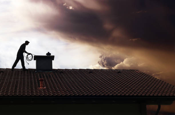 A chimney sweep cleans the chimney on a house roof while thunderclouds gather